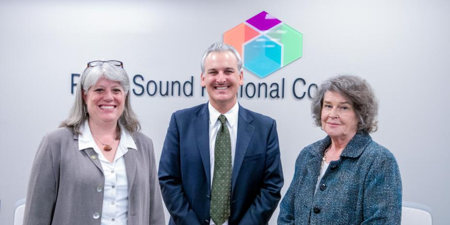Three people standing in front of a wall with the PSRC sign