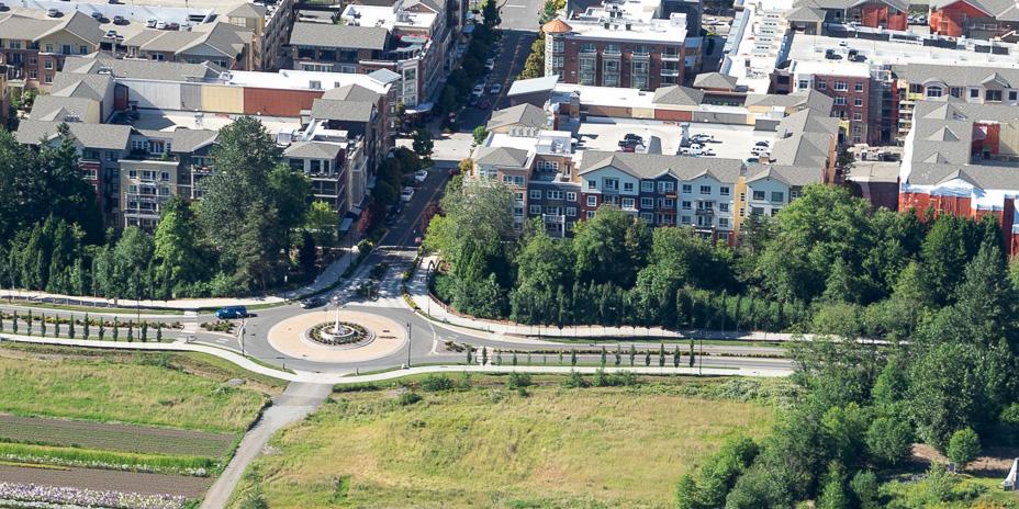 An aerial view of a roundabout. One side of the street is an open space, the other is city development.