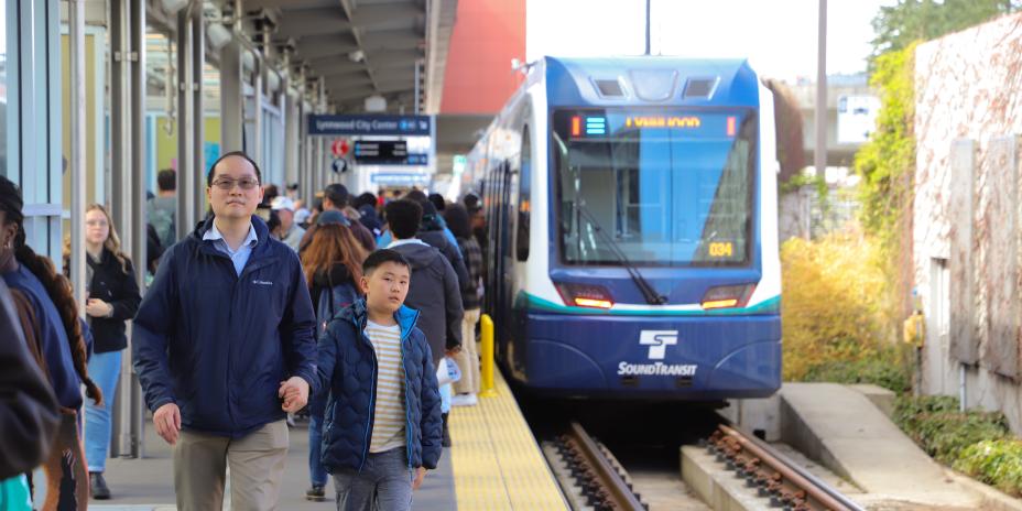 A son and father walking on a train platform as the train pulls in. 